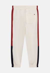Pantaloni jogger crema chiaro con strisce laterali rosse e blu navy, vita elastica e tasca posteriore. Realizzati in un tessuto morbido e confortevole.