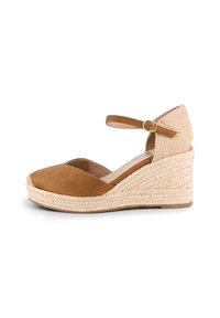 Sandal de cuña de ante marrón con tacón de cuerda trenzada, punta abierta y tira para el tobillo asegurada por una hebilla metálica.
