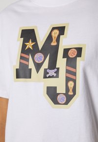 Lettres en blocs noir et beige "MJ" sur tissu blanc, décorées de ballons de basket, trophées, une étoile et des battes de baseball croisées.