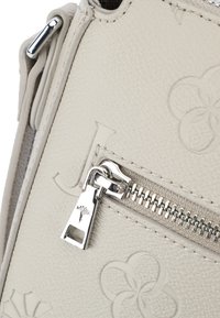 Borsa a tracolla in pelle beige chiaro con motivi floreali in rilievo, hardware della cerniera in argento e un piccolo etichetta del designer sul tirante della cerniera.
