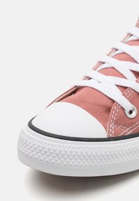 Růžové plátěné sneakers s bílým gumovým špičkou a texturovanou bílou podrážkou. Mají bílé tkaničky a švy, což dokresluje klasický design.