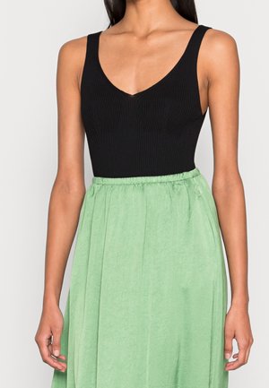 Kvinde iført en sort ribbet ærmeløs top med V-hals kombineret med et højtaljet lysegrønt tekstureret nederdel.