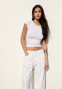 White cropped t-shirt with short sleeves paired with loose-fitting white trousers. Smooth texture, minimal design, and relaxed silhouette.