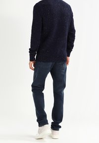 Navy knitted sweater with textured pattern, paired with dark blue jeans and light sneakers. Sweater has ribbed cuffs and hem.
