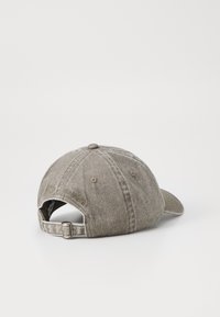 En bomull baseball cap i dempet grå med en teksturert finish. Har en buet skjerm og justerbar stropp bak, merket "SANSIZE."