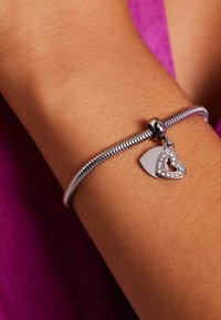 Silver bracelet with a flexible design, featuring a heart charm adorned with clear stones and a smooth metallic surface.