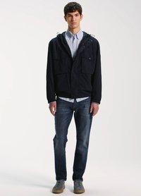 Laivastonsininen huppari, jossa on huppu ja etutaskut, käytetty vaalean raidoitetun paidan ja tummien farkkujen päällä, yhdistetty harmaisiin kenkiin.