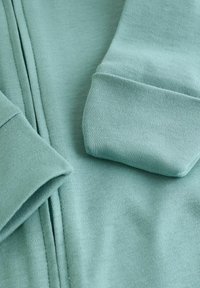 Sweatshirt en coton vert clair plié, montrant des poignets côtelés et une texture de tissu douce.