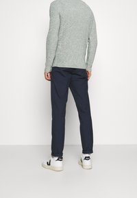 Pull en tricot gris clair, pantalon bleu marine et baskets blanches avec des accents noirs. La tenue présente une coupe décontractée et une texture subtile.