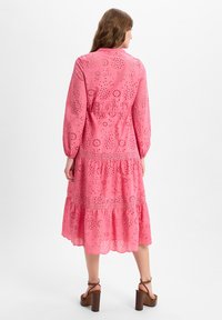 Rosa, langärmliges Kleid mit Durchbr embroidery, einem gestuften Rock und einem gewellten Saum, kombiniert mit braunen Plateausandalen.