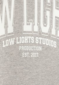 Sudadera de algodón gris con texto blanco en negrita: "LOW LIGHTS STUDIOS PRODUCTION EST. 2017" con un diseño de fuente colegial.
