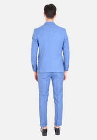 Completo azzurro chiaro in tessuto testurizzato con una vestibilità sartoriale, caratterizzato da una giacca monopetto e pantaloni slim, indossato con scarpe nere.