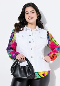 Chaqueta de mezclilla blanca con botones plateados, mangas largas de patrón colorido y un bolso negro texturizado. Combinada con leggings negros brillantes.