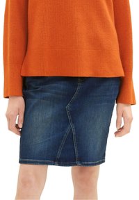 Džínová sukně v tmavě modré barvě s tužkovým střihem a šikmými švy. Kombinována s oranžovým žebrovaným svetrem, který zvýrazňuje detaily horní části a pasu.