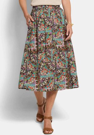 Frau trägt einen bunten, gemusterten Midirock mit Taschen, hellbraune Sandalen mit offenen Zehen, ein beiges Oberteil und ein goldenes Armband am rechten Handgelenk.