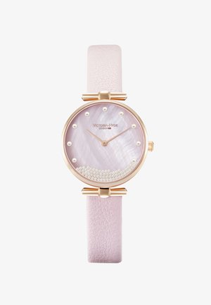 Okrugli zlatni sat s ružičastom kožnom narukvicom, brojčanik od biserne školjke i srebrnim perlama kao naglascima. Ima jednostavne oznake sati.