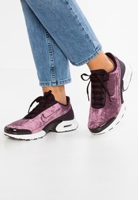 Scarpe Nike con una tomaia testurizzata viola e accenti scuri, suola nera e bianca, e sistema di allacciatura tradizionale.