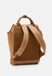 Sac à dos en tissu marron avec poignée supérieure robuste, bretelles réglables et poches latérales. Texture lisse avec accents contrastants. Design polyvalent.
