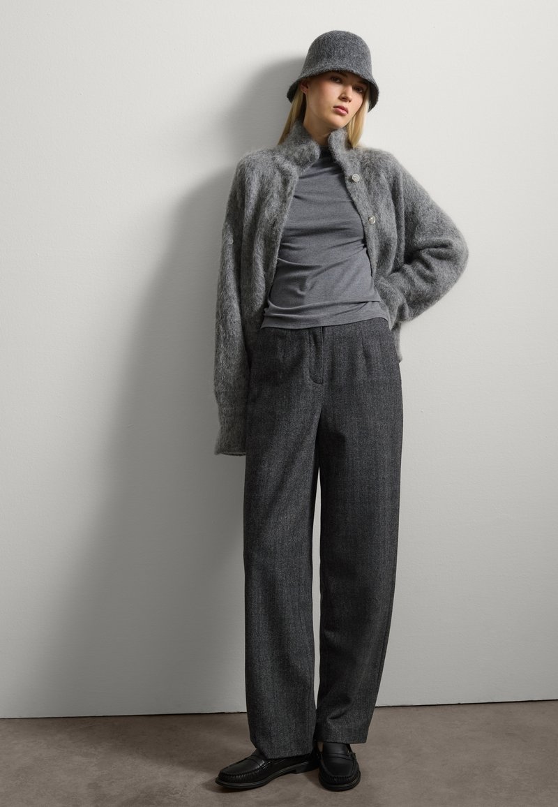 Cardigan gris esponjoso, top gris ajustado, pantalones gris de corte a medida y zapatos negros. Un sombrero de lana gris a juego completa el look.