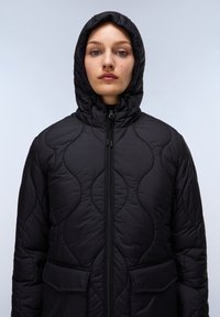 Svart vadderad jacka med quiltat mönster, med huva, framdragkedja och två sidofickor. Slät textur och varmt material.