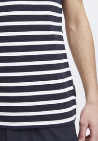 Navy and white striped tank top made of textured fabric. Features a rounded hem and a small brand label on the side.