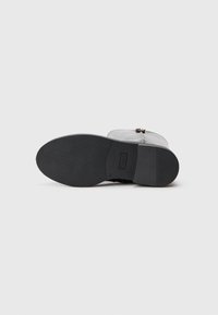 Botte de cheville en cuir noir avec semelle texturée, fermeture éclair et accents minimalistes. La semelle a une finition lisse et une légère voûte pour un soutien optimal.