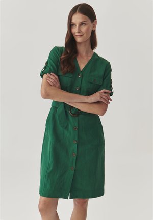Green linen dress with a V-neck, short sleeves, two breast pockets, and a tied waist belt. Features large, round buttons down the front.