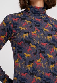 Polotröja med långt ärm i mörk tyg som har ett färgglatt hästmönster i gult, rött och svart, med en figurnära silhuett.
