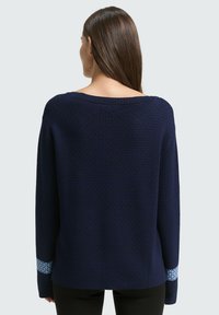 Maglione blu navy con motivo testurizzato, ampio scollo a barca e dettagli a contrasto in azzurro chiaro sui polsini. Vestibilità comoda, maniche lunghe.