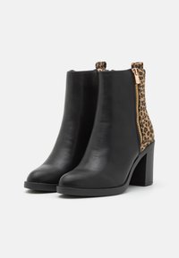 Botas de tobillo de cuero negro con una parte trasera de estampado de leopardo y detalle de cremallera dorada. Presenta un tacón grueso y un diseño de punta redonda.