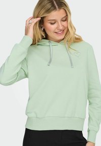 Felpa verde menta con cappuccio e coulisse argentata. Presenta un piccolo ricamo a forma di cuore e polsini e orlo a costine. Realizzata in tessuto morbido.