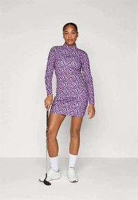 Φόρεμα μακρυμάνικο, με λεοπάρ μοτίβο σε μωβ από ελαστικό ύφασμα, με ψηλό λαιμό και στενή εφαρμογή. Συνδυασμένο με λευκά παπούτσια γκολφ και κάλτσες.