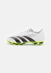 Botas de fútbol blancas con rayas negras, parte superior perforada, cuello gris y suela de un vibrante color verde con tacos moldeados para tracción.