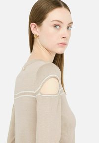 Beiger Strickpullover mit Schulterausschnitten, weißen horizontalen Streifen, rundem Hals und subtilen goldenen Hardwaredetails auf der Rückseite.