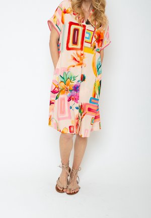 Bloemenjurk in pastelroze, met abstracte vormen in felle kleuren, korte mouwen, zijkanten met zakken en een ontspannen pasvorm. Sandalen met strikken.