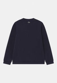 Mörkblå sweatshirt i bomull. Har långa ärmar, rund halsringning och ribbade muddarna. Anmärkningsvärt grönt logotyp på baksidan av halsringningen.