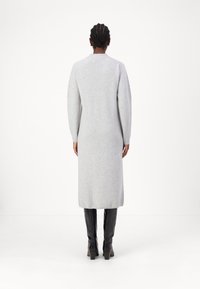 Robe en tricot grise longue avec un col rond et des manches longues. Texture lisse, arrivant sous le genou, associée à des bottes noires brillantes au genou.