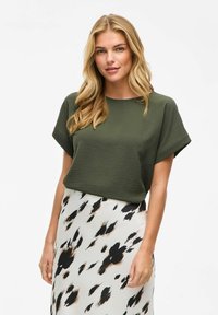 Haut à manches courtes vert olive avec une coupe décontractée, associé à une jupe fluide ornée d'un motif tacheté noir et marron sur un fond clair.