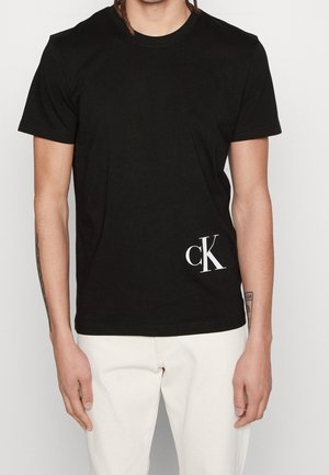 Sort bomulds-t-shirt med rund halsudskæring, korte ærmer og et hvidt "cK" logo nederst til venstre.