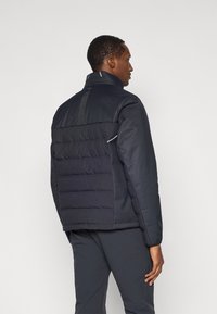 Casaco puffer de cor azul marinho escuro com uma seção superior texturizada e painéis inferiores lisos. Possui um colarinho alto e elementos refletivos nas costas.