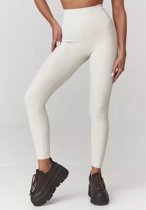 Wysokie, kremowe legginsy ribbed o dopasowanym kroju; w połączeniu z ciemnobrązowymi butami na platformie. Gładka faktura, bez widocznych wzorów.