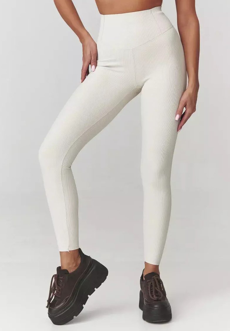 Wysokie, kremowe legginsy ribbed o dopasowanym kroju; w połączeniu z ciemnobrązowymi butami na platformie. Gładka faktura, bez widocznych wzorów.