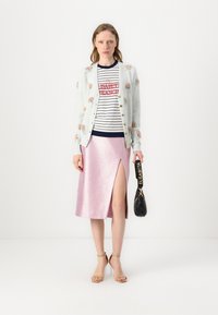 Cardigan azul claro con bordado floral, blusa a rayas en azul marino y blanco, falda rosa brillante con abertura, y bolso negro con correa. Sandalias beige.