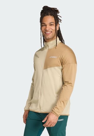 Beige en tan zip-up jack met een hoge kraag, een gestructureerd lichaam en gladde mouwen. Bevat het TERREX-logo op de borst.