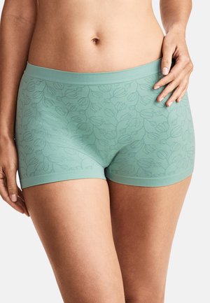 Frau trägt türkisfarbene nahtlose Boyshorts mit dezentem Blumenmuster und steht mit einer Hand an der Hüfte.