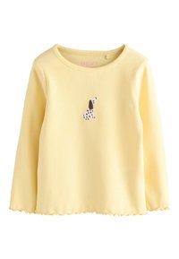 Žuta rebrasta majica dugih rukava s valovitim rubom i malim izvezenim dizajnom psa na prednjoj strani. Izrađena od mekanog pamuka.
