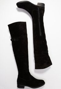 Stivali neri in suede alti fino al ginocchio con una finitura testurizzata, dotati di zip laterale e dettaglio con cinturino, e un design a tacco basso.