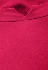 Tessuto a maglia fucsia con una superficie liscia, scollatura rotonda e un sottile dettaglio di cucitura vicino al colletto, che enfatizza un design minimalista.