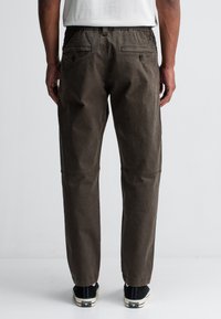 Bruine katoenen broek met een elastische tailleband, rechte pijpen en twee achterzakken. Kenmerkt zich door stiksel-details en een klassieke snit.