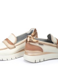 Chaussures slip-on légères avec une combinaison de couleurs crème et bronze. Tige en cuir lisse, col rembourré et semelle en caoutchouc avec un motif.